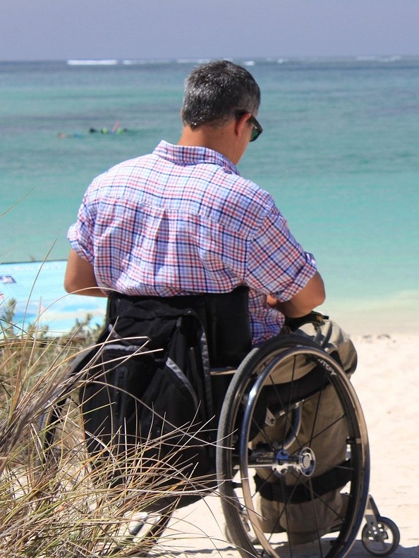 Modern tekerlekli sandalyesi ile günlük kıyafetleri ile deniz kenarında oturan bir adam